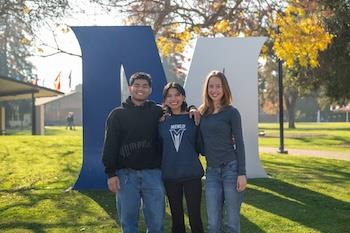 Group of Menlo College students posing by the campus 'M' sculpture on the quad.
