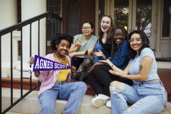 students smiling with 'agnes scott' sign on campus steps