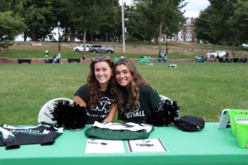 two students at a promotional table, smiling