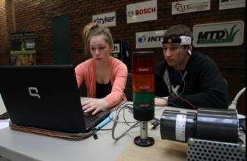 two students working on a project with a computer and equipment