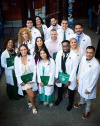 graduates in white coats holding green diplomas