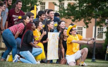 group of students smiling for a selfie on campus lawn