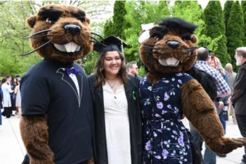 graduate posing with two beaver mascots at outdoor ceremony