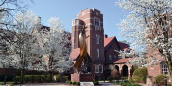 brick building with clock tower and blooming trees on campus