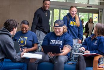 students sitting and laughing with laptops, wearing mount st. joseph university apparel