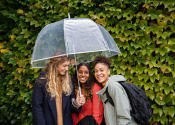 three students under umbrella, smiling
