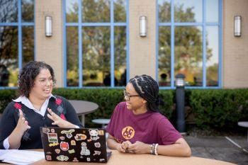 two students studying outside with laptop