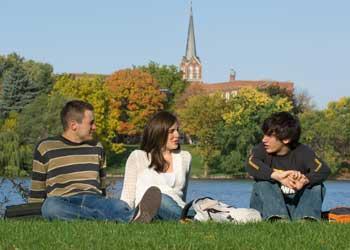 students sitting on grass near water with trees